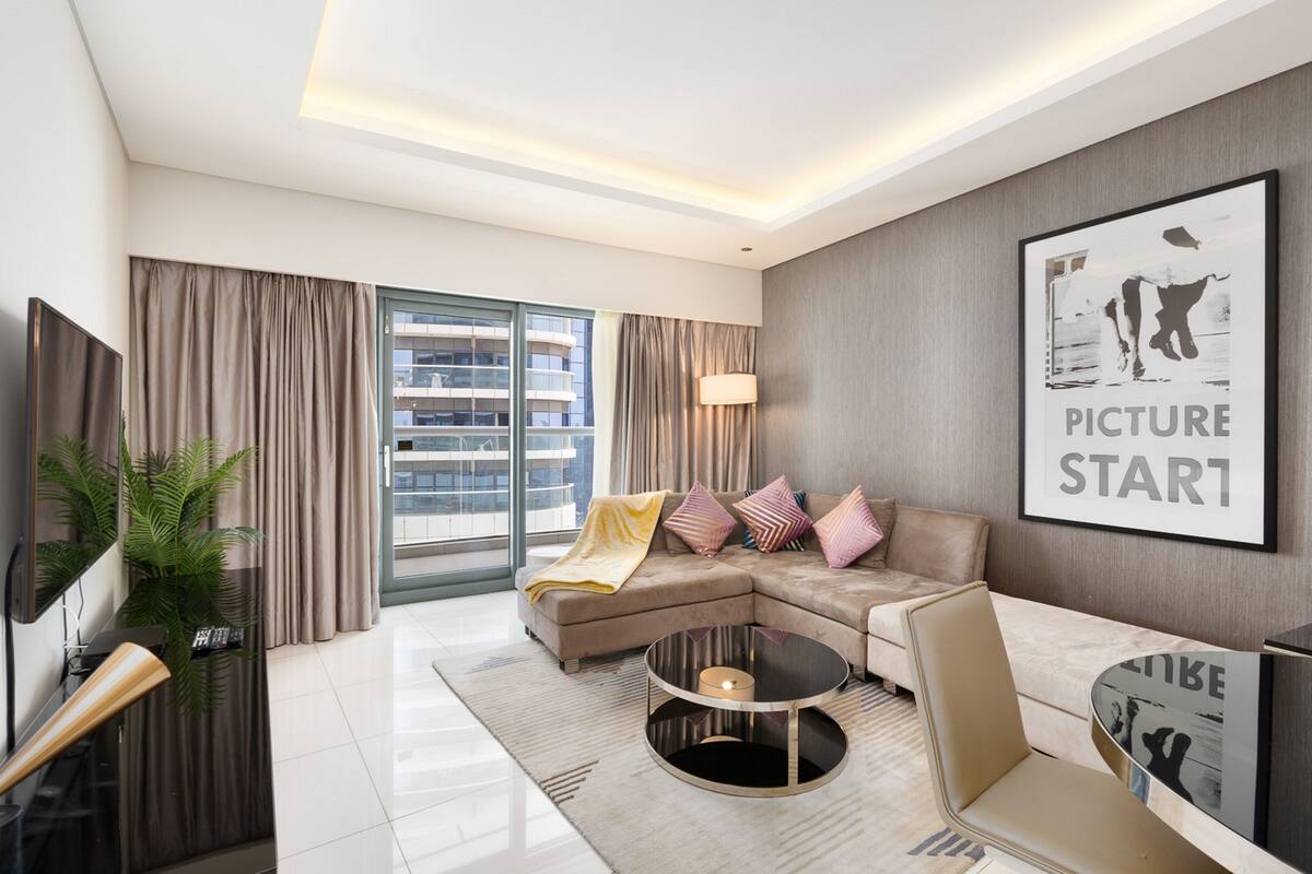 A modern living room with a sectional sofa, a round coffee table, and a large window with curtains.