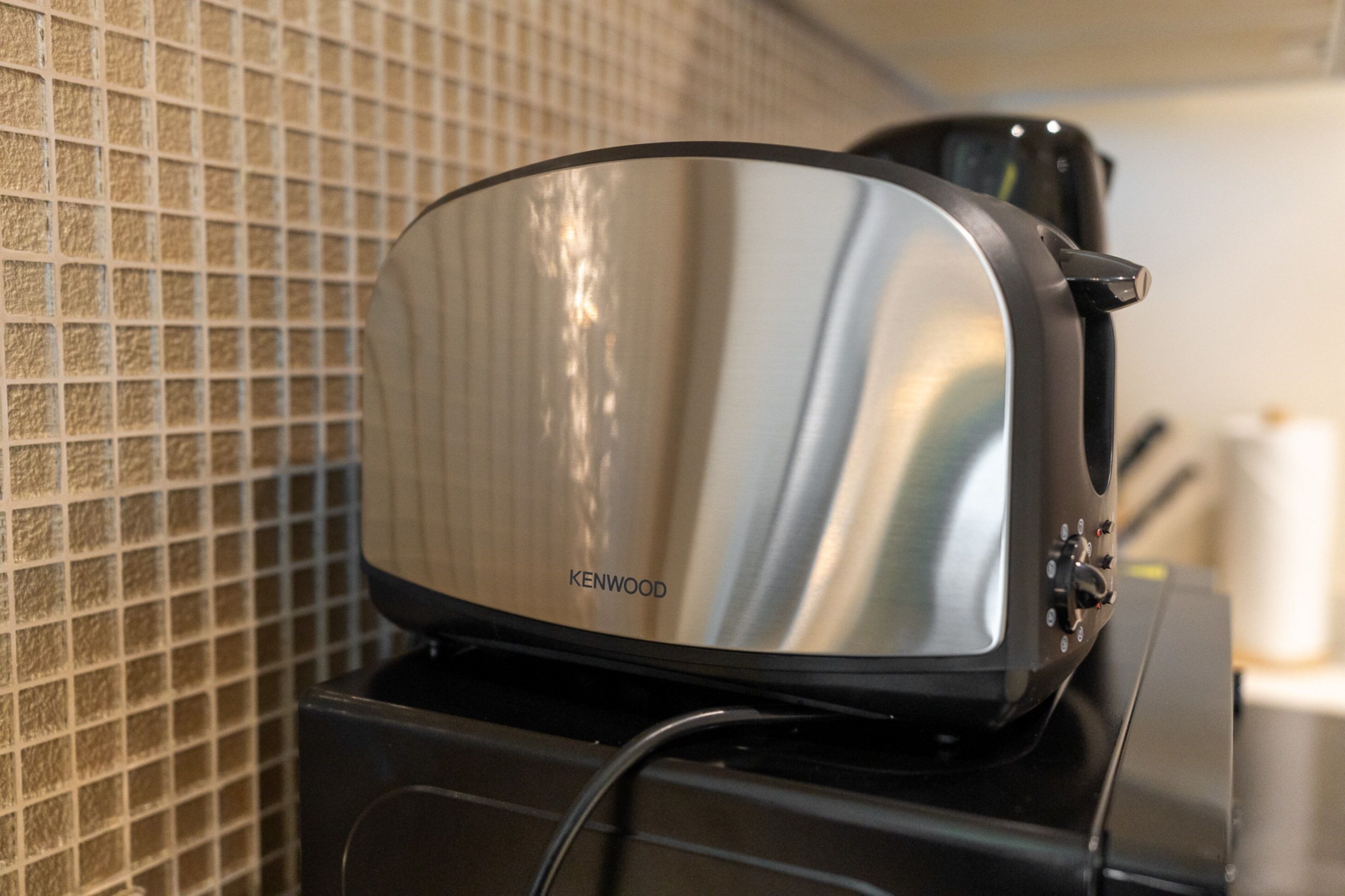 A Kenwood audio system on a black stand with a tiled wall in the background.