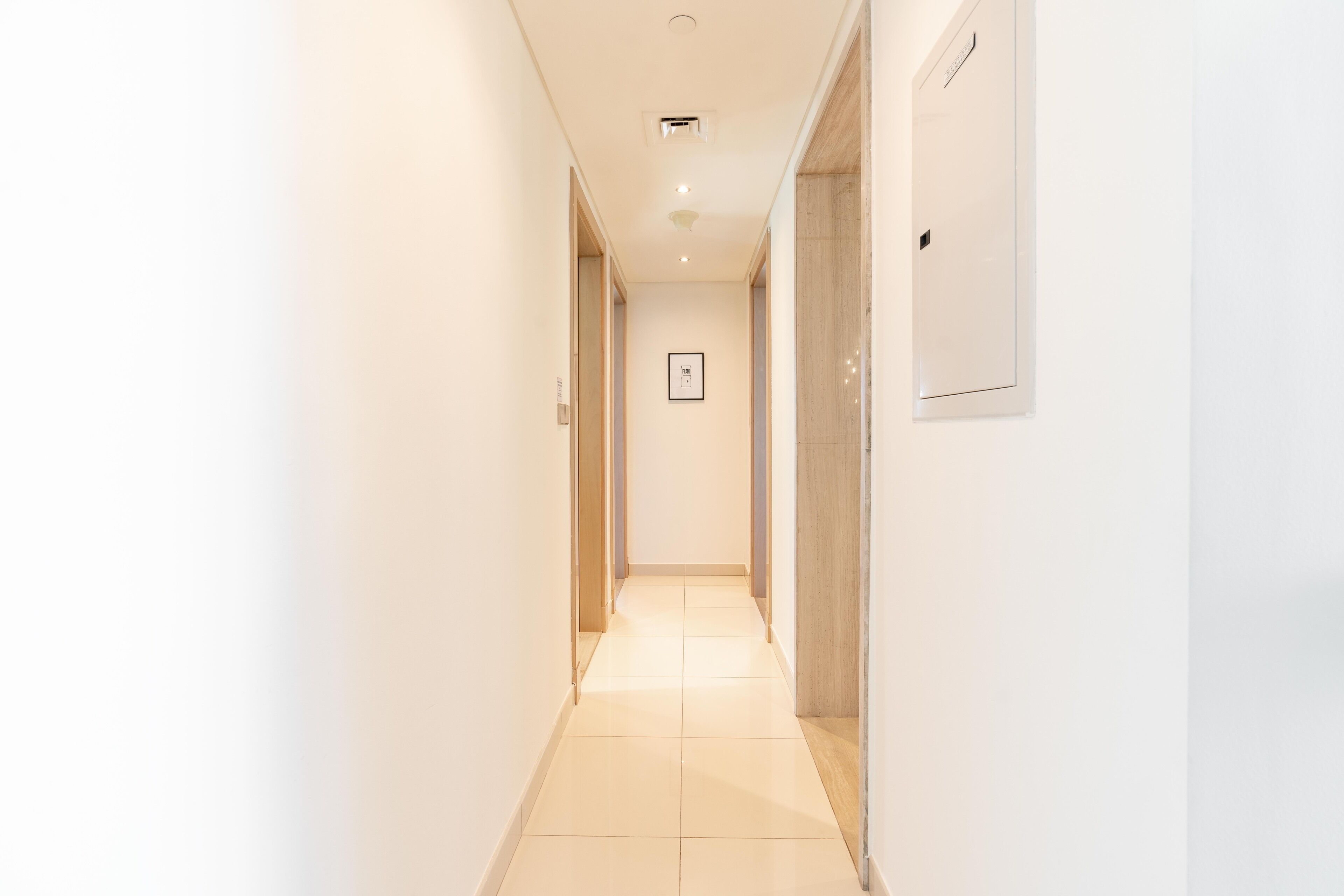 A narrow, well-lit hallway with a tiled floor, leading to a door at the end.