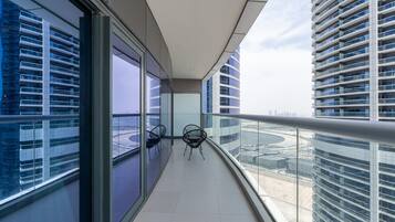 A modern balcony with glass railings, a view of a cityscape, and two chairs.