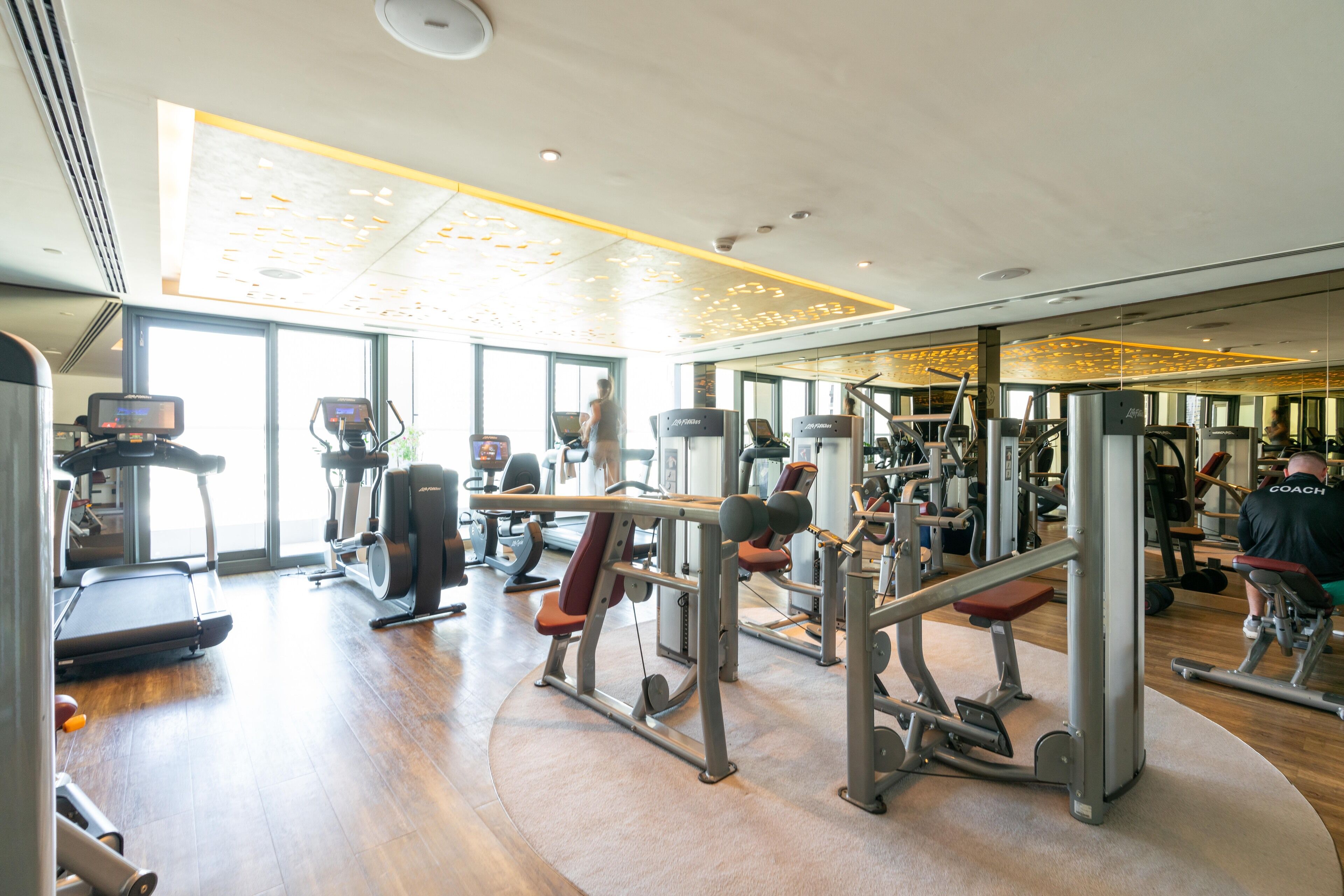 Une salle de sport équipée de tapis de course, d’appareils de musculation et d’un mur entièrement recouvert de miroirs.