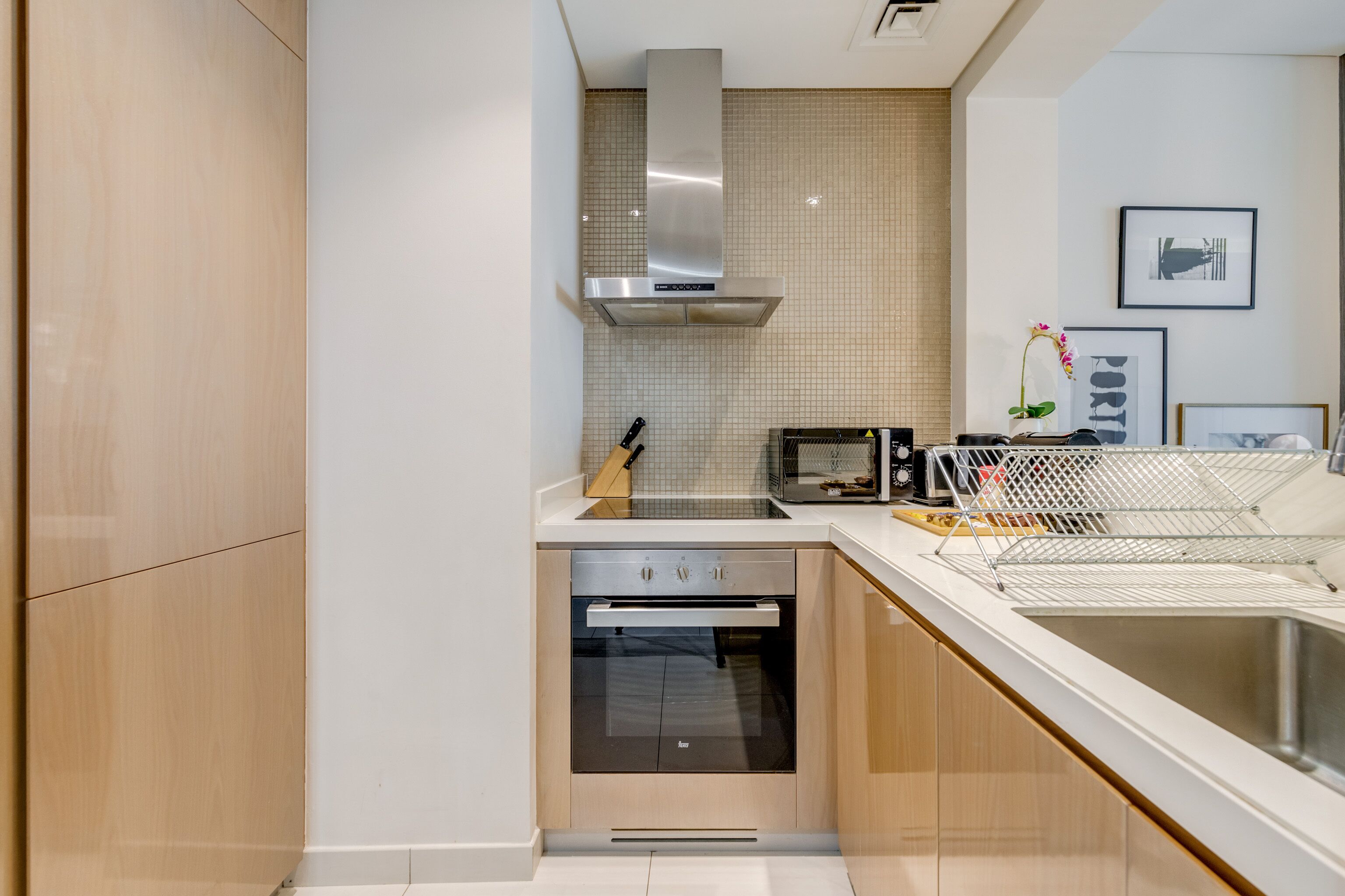 Ett modernt kök med en inbyggd ugn, en fläktkåpa i rostfritt stål och en vit bänkskiva.