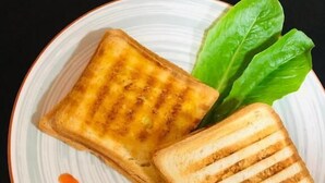 Two grilled sandwiches on a plate with a leaf garnish and a sauce drizzle. - The Friends Hotel (Yerevan)