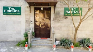 A hotel entrance with a large wooden door, steps leading up to it, and two signs above the door. - The Friends Hotel (Yerevan)