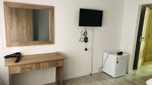 A room with a wooden desk, a mounted television, and a white refrigerator. - The Friends Hotel (Yerevan)