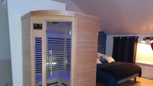 Eine Sauna mit digitaler Anzeige, ein Bett mit Kissen und ein Fenster mit Vorhängen.