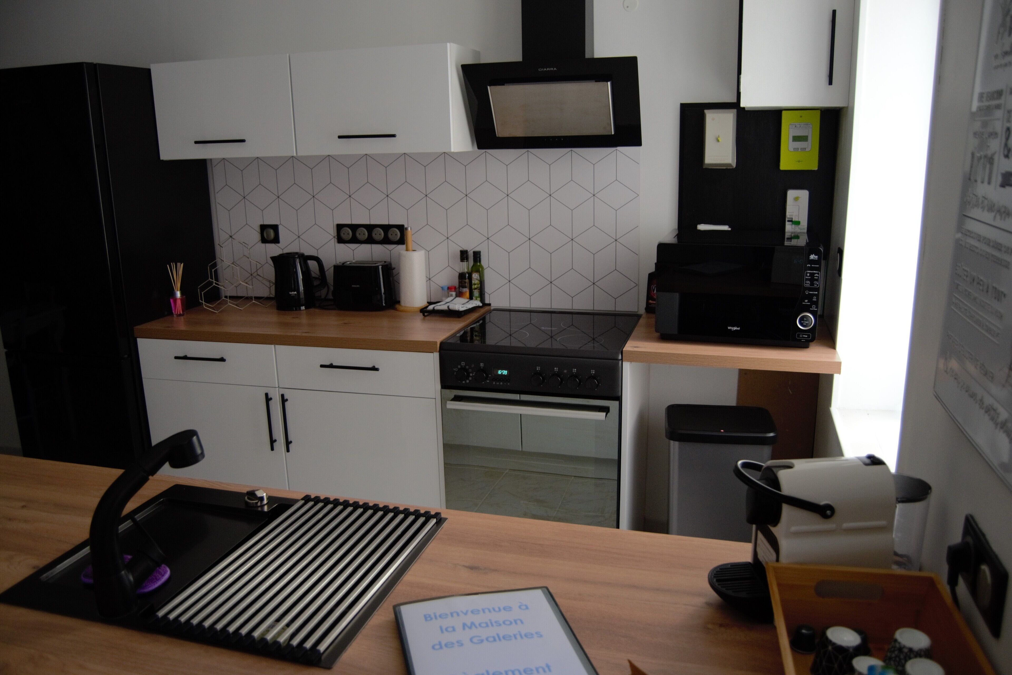 Una cocina moderna con gabinetes blancos, una estufa negra y un microondas. Hay una cafetera y un hervidor en la encimera.