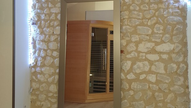 Ein Zimmer mit Steinwand, Holztür und Spiegel, der eine Holzbalkendecke reflektiert.