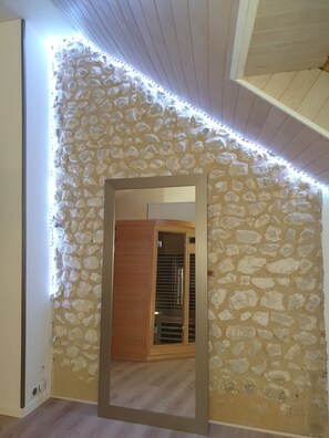 Een kamer met een stenen muur, een houten deur en een spiegel die een houten plafond weerspiegelt.