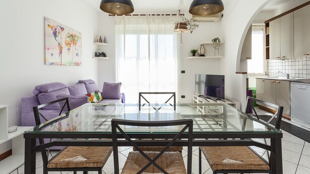 Ein modernes Wohnzimmer mit einem Glastisch, einem violetten Sofa und zwei Pendelleuchten.