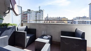 Eine Dachterrasse mit Korbmöbeln, einer Satellitenschüssel und Blick auf Stadtgebäude.