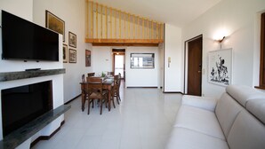 A spacious living room with a high ceiling, a fireplace, a dining area, and a sofa. - Residenza Airone (Polpenazze del Garda)