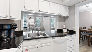 Una cocina moderna con armarios blancos, encimera negra y cafetera.
