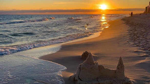 Una playa con un castillo de arena y el océano al atardecer.