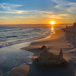A beach with a sandcastle and the ocean at sunset.