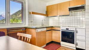 Una cocina con armarios de madera, lavavajillas, horno y ventana con vista a la montaña.