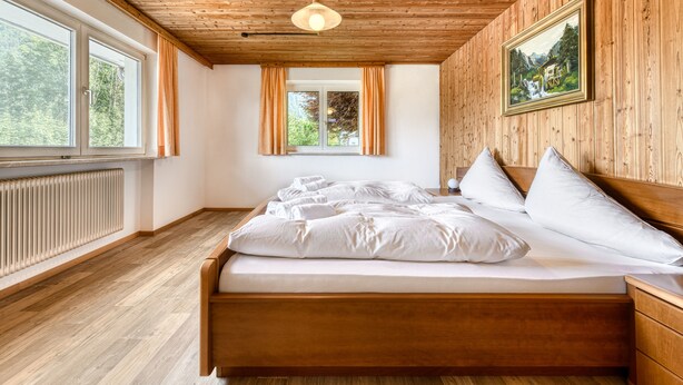 Un dormitorio con paneles de madera, una cama, un radiador y un ventanal grande.