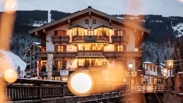 A multi-story hotel with a prominent entrance, balconies, and a ski slope in the background. - Geniesserhotel Hubertus (Filzmoos)