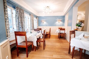 Un espace repas comprenant plusieurs tables et chaises, un lustre et des appliques murales.