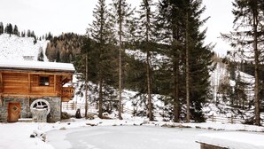 A wooden cabin with a stone foundation, surrounded by snow-covered ground and tall pine trees. - Geniesserhotel Hubertus (Filzmoos)