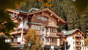 A traditional wooden building with multiple balconies and large windows, surrounded by trees and a mountainous backdrop. - Geniesserhotel Hubertus (Filzmoos)