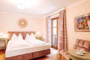 Une chambre d’hôtel avec un grand lit, une table ronde avec des tasses, un tableau et une fenêtre avec des rideaux.