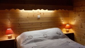 Une pièce chaleureuse avec des boiseries, un lit recouvert d’une courtepointe à motifs et deux lampes de chevet.