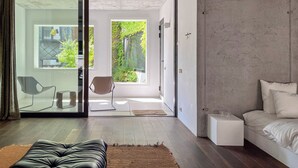Un dormitorio moderno con un gran ventanal corredera que da a un balcón, un sofá, una mesita de noche y una cama.