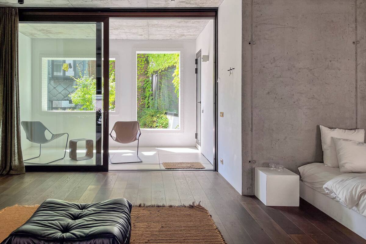 Ein modernes Schlafzimmer mit einem großen Schiebeglastür, die auf einen Balkon führt, einer Couch, einem Nachttisch und einem Bett.