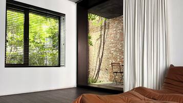 A modern bedroom with a large window, a view of a brick wall, and a cozy bed.