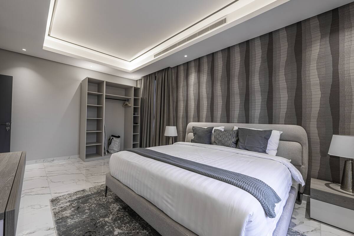 A modern bedroom with a large bed, built-in wardrobe, and a marble floor.
