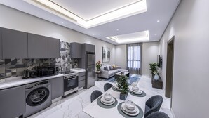 Eine moderne Küche mit Einbaugeräten, ein Essbereich mit Tisch für vier Personen und ein Wohnzimmer mit Sofa und Fernseher.