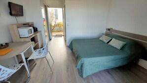 Une petite chambre comprenant un lit, un bureau avec une chaise, un four à micro-ondes et un téléviseur fixé au mur.