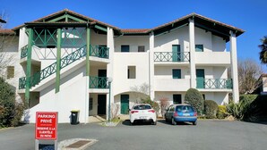 Un immeuble à plusieurs étages, doté d’une façade blanche et de touches de vert, avec des balcons et un escalier.