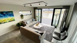A modern living room with a sofa, coffee table, and a chair. There is a large window with a view of a body of water and a building. - Water Villa in Balk With Private Jetty (Balk)