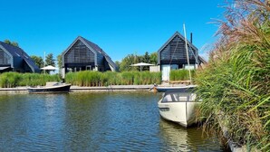 A canal with two modern buildings, a boat docked, and lush greenery. - Water Villa in Balk by Slotermeer Lake (Balk)