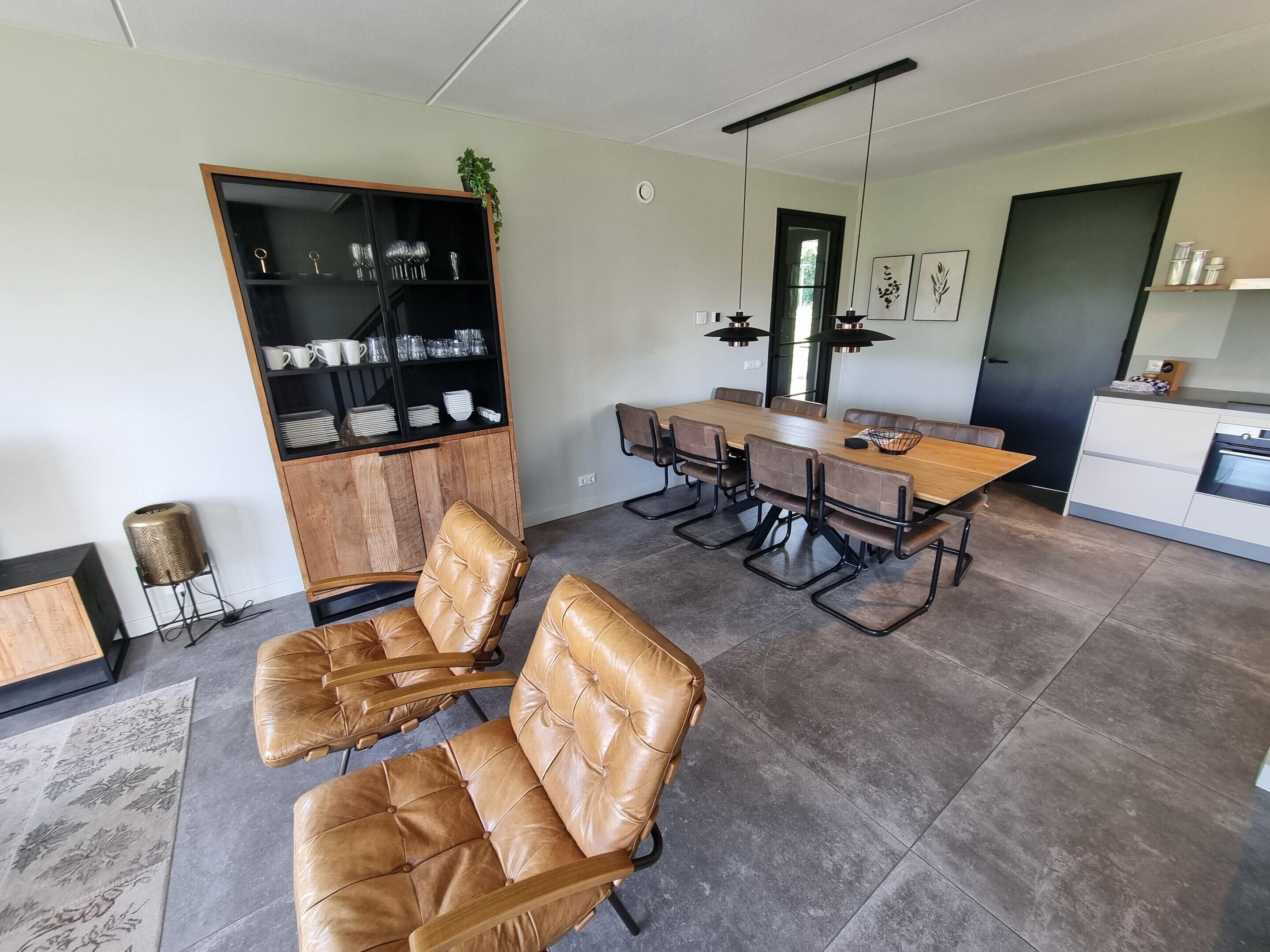A modern dining area with a wooden table and leather chairs, a built-in bookshelf, and a kitchen area with a stove.