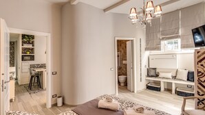 A bedroom with a bed, a TV, a chandelier, and a bathroom visible through an open door.