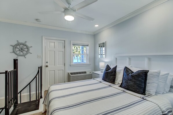 A bedroom with a bed, a ceiling fan, a window, and a door. - Condo Steps from Beaches, Heated Pool Access (Tybee Island)