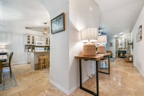 A modern kitchen with white cabinets, a dining area with a table and chairs, and a hallway leading to a living room with a fireplace.