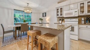 Uma cozinha com armários brancos, bancada de granito e área de jantar com mesa e cadeiras.