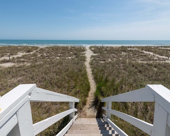 A wooden boardwalk leading to a beach with a clear view of the ocean.