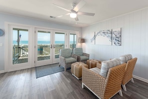 A room with wicker furniture, a ceiling fan, and a view of the ocean through glass doors.