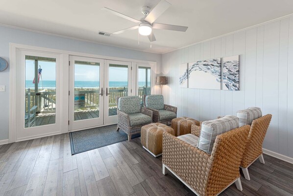 A room with wicker furniture, a ceiling fan, and a view of the ocean through glass doors.