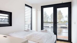 Camera d'albergo moderna con due letti, un comodino e un'ampia finestra con persiane.