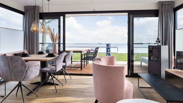 Zona pranzo moderna con vista sul mare, con tavolo in legno, sedie grigie e una poltrona rosa.