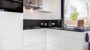 Una cucina moderna con mobili bianchi, un piano di lavoro nero e una finestra vista alberi e un edificio.