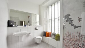 A modern bathroom with a white sink, toilet, and vanity. There is a large mirror above the sink and a window with blinds. - The Meadowpark (Stirling)