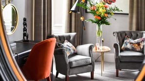 A modern hotel room with two grey armchairs, a red chair, a small round table, and a floral vase. - The Meadowpark (Stirling)