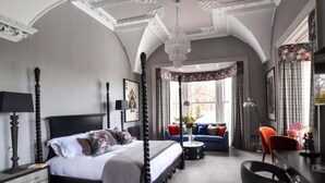 A four-poster bed with a canopy, a desk with a chair, and a sofa in a room with a high ceiling and ornate moldings. - The Meadowpark (Stirling)